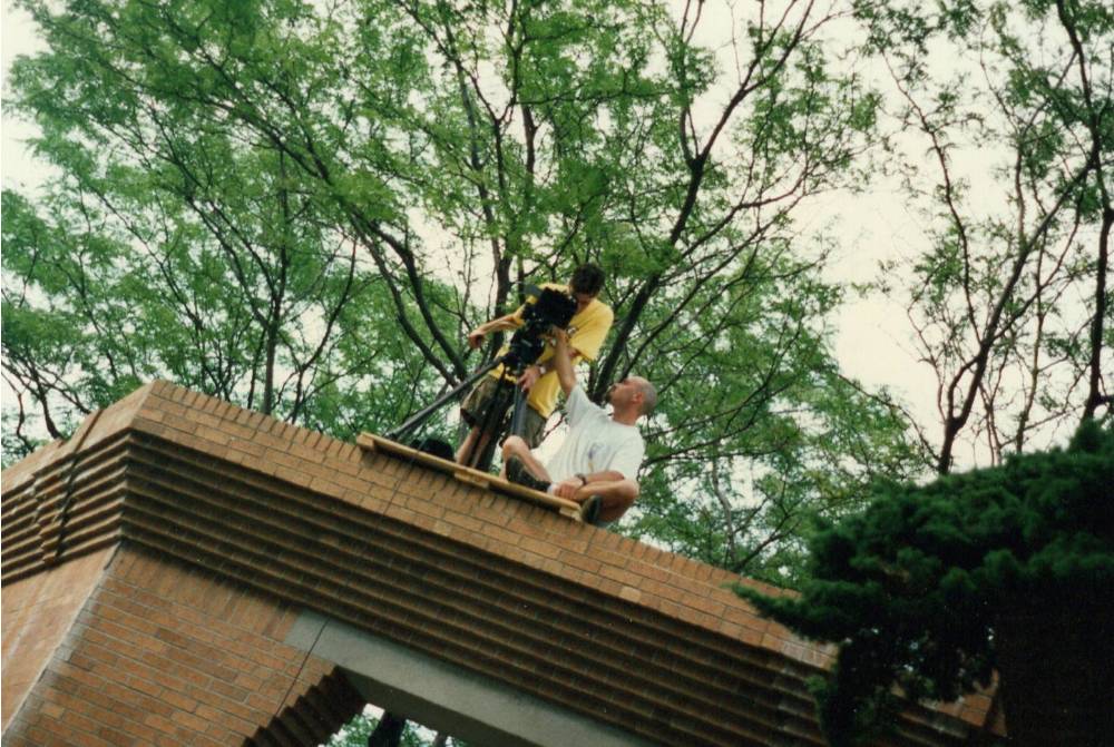 Two members of camera team operating a camera on a tripod on top of a roof.